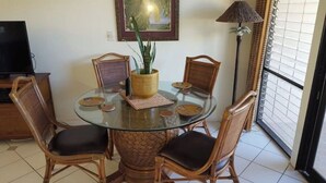 Una mesa redonda de cristal con sillas de mimbre, un mantel tejido y una planta en maceta.