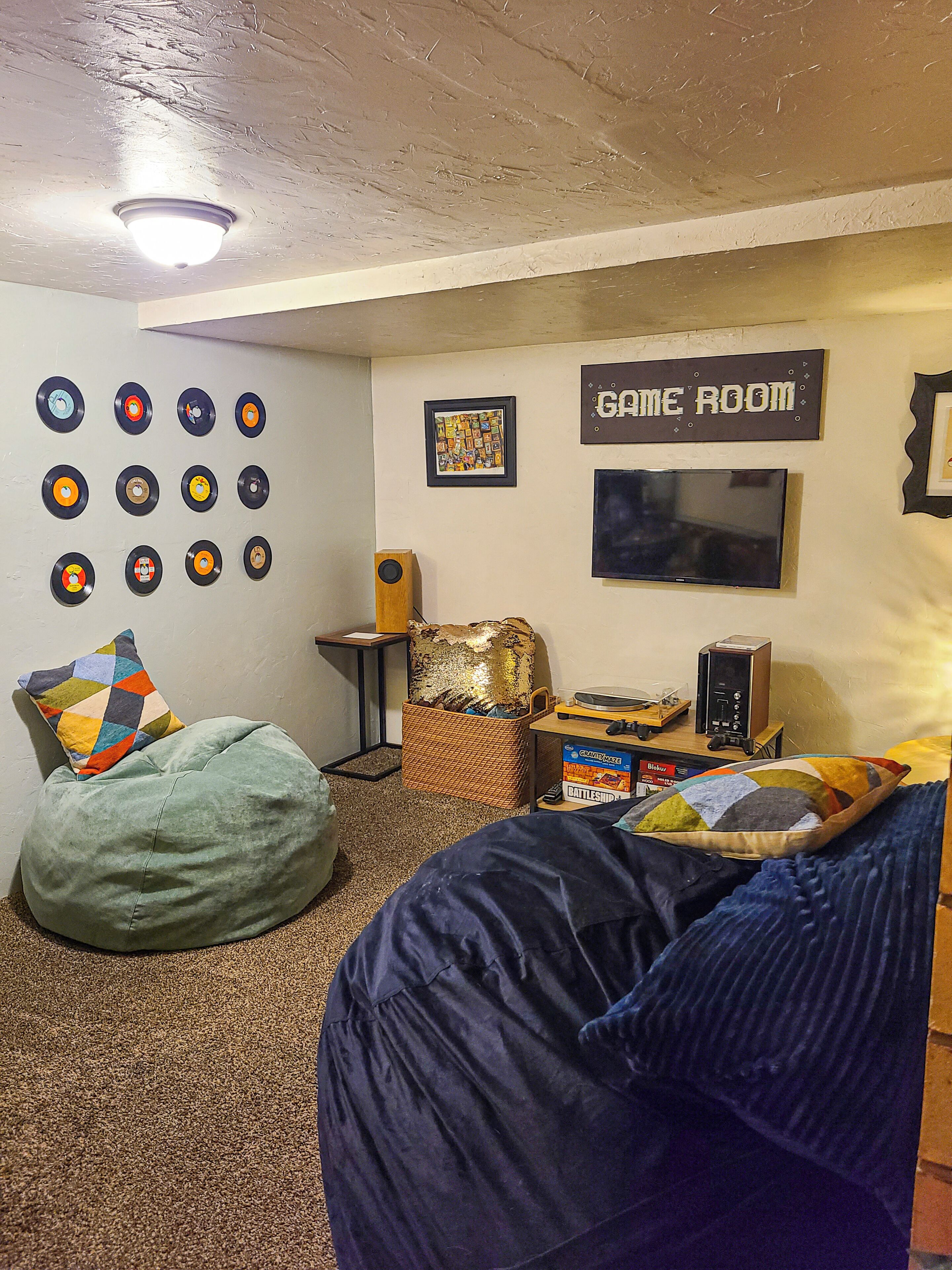Une pièce avec un fauteuil en forme de sac de haricots, une console de jeux et un mur décoré de disques vinyle.