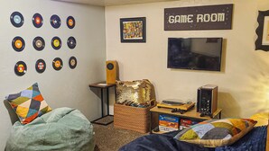 A room with a bean bag chair, a gaming console, and a wall decorated with vinyl records. - 3BR Near SLC & Airport +Game Room | Basement level (West Valley City)