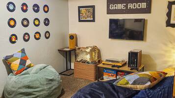 Une pièce avec un fauteuil en forme de sac de haricots, une console de jeux et un mur décoré de disques vinyle.