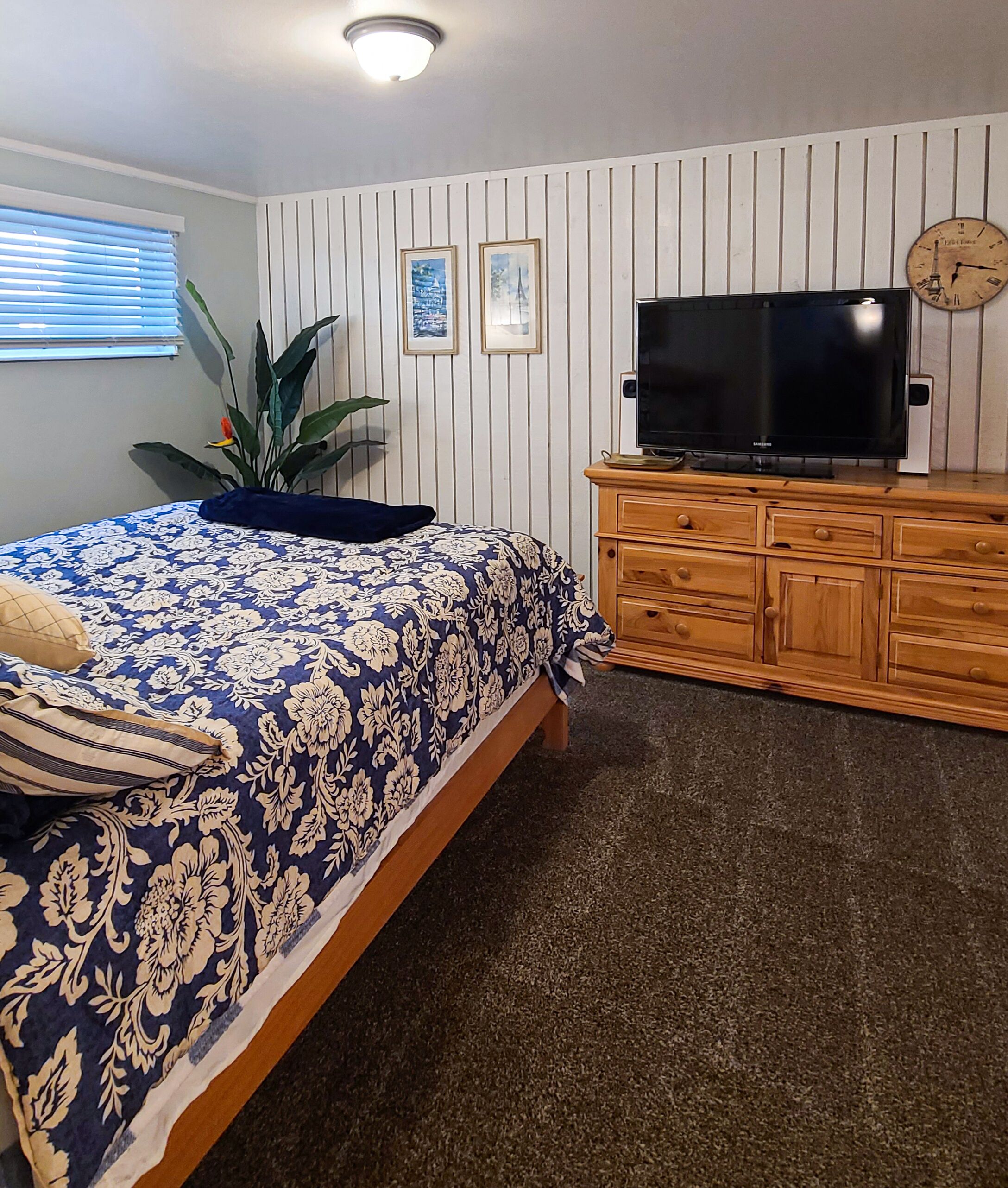 A bedroom with a bed, a television, a clock, and a plant.