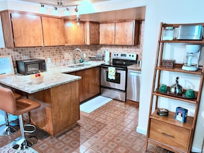 Una cocina con armarios de madera, microondas, estufa, lavabo y cafetera.