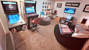 Uma sala de jogos com duas máquinas de pinball, uma poltrona de saco e uma TV exibindo um jogo de corrida.