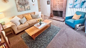 A living room with a sofa, a coffee table, a fireplace, and a blue armchair. - 3BR Near SLC & Airport +Game Room | Basement level (West Valley City)
