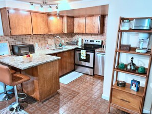 Una cocina con armarios de madera, microondas, estufa, lavabo y cafetera.