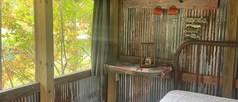 Una cabaña rústica con una cama de madera, una mesita y un estante con adornos.