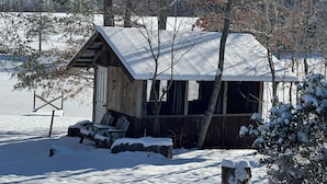 A wooden cabin with a snow-covered roof, surrounded by trees and a snowy landscape.