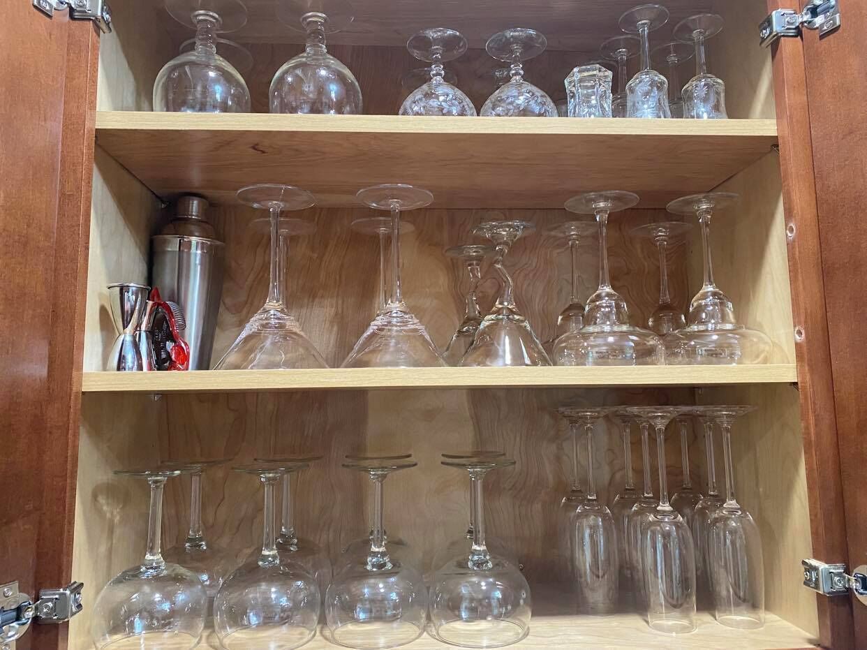 Un meuble en bois doté d’étagères où sont rangés divers objets en verre, notamment des verres à vin et des carafes.