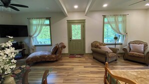 A spacious living room with a wooden floor, two sofas, a curved chair, a TV, and a ceiling fan.