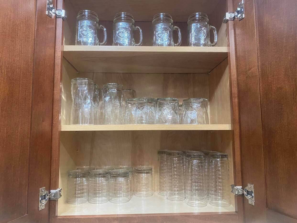 Een houten kast met drie planken, elk gevuld met glazen bekers en glaasjes.