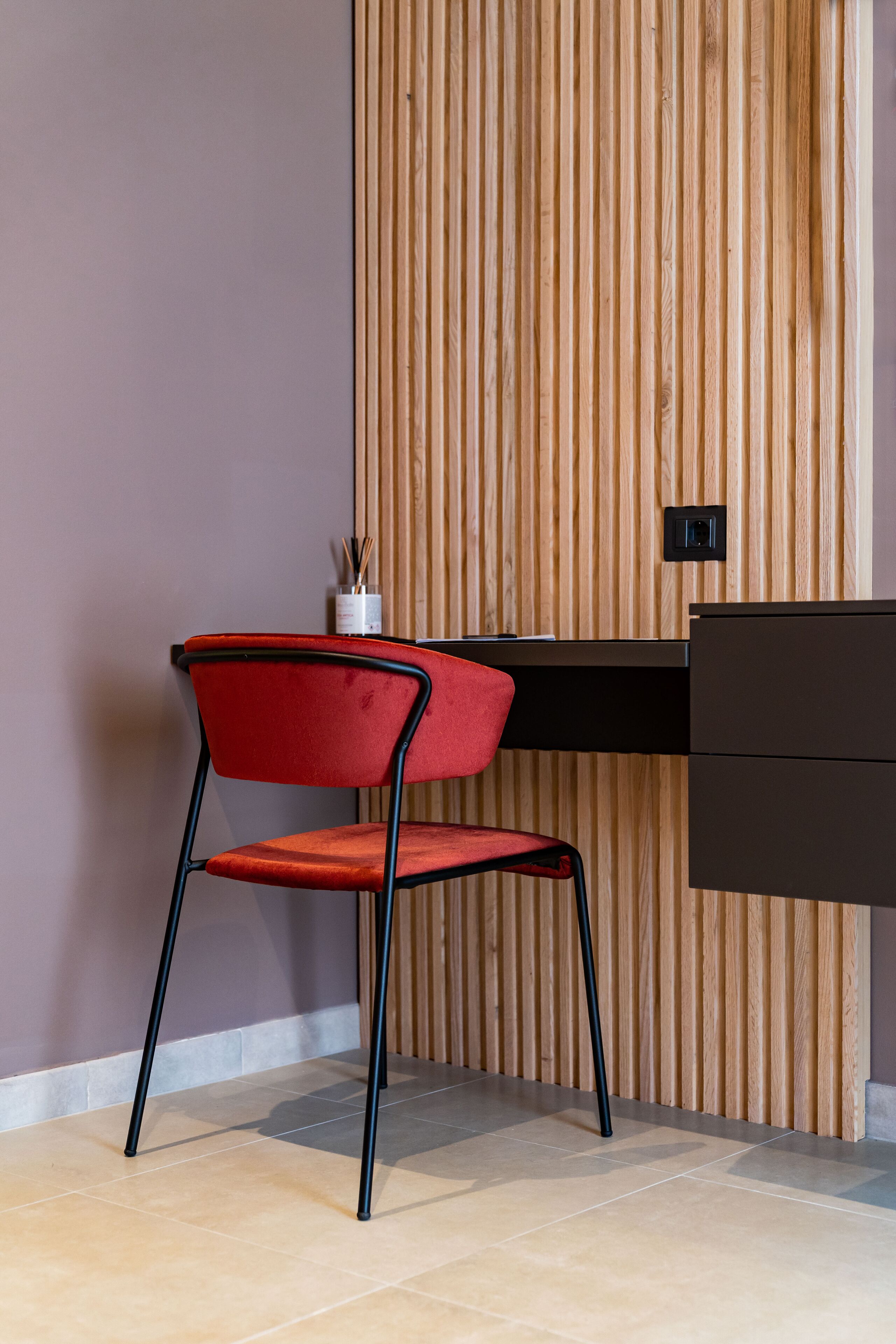 Un espace de bureau moderne avec une chaise rouge, un mur en lambris de bois et un bureau noir.