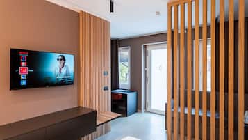 Un salon moderne avec un téléviseur à écran plat fixé au mur, un séparateur en bois, un bureau avec une chaise et un escalier menant à un autre niveau.