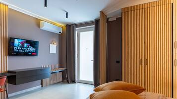 Ein modernes Hotelzimmer mit flachbildfernseher an der Wand, einem Schreibtisch mit Stuhl, einem Bett mit zwei Kissen und einem Kleiderschrank mit vertikalen Lamellen.