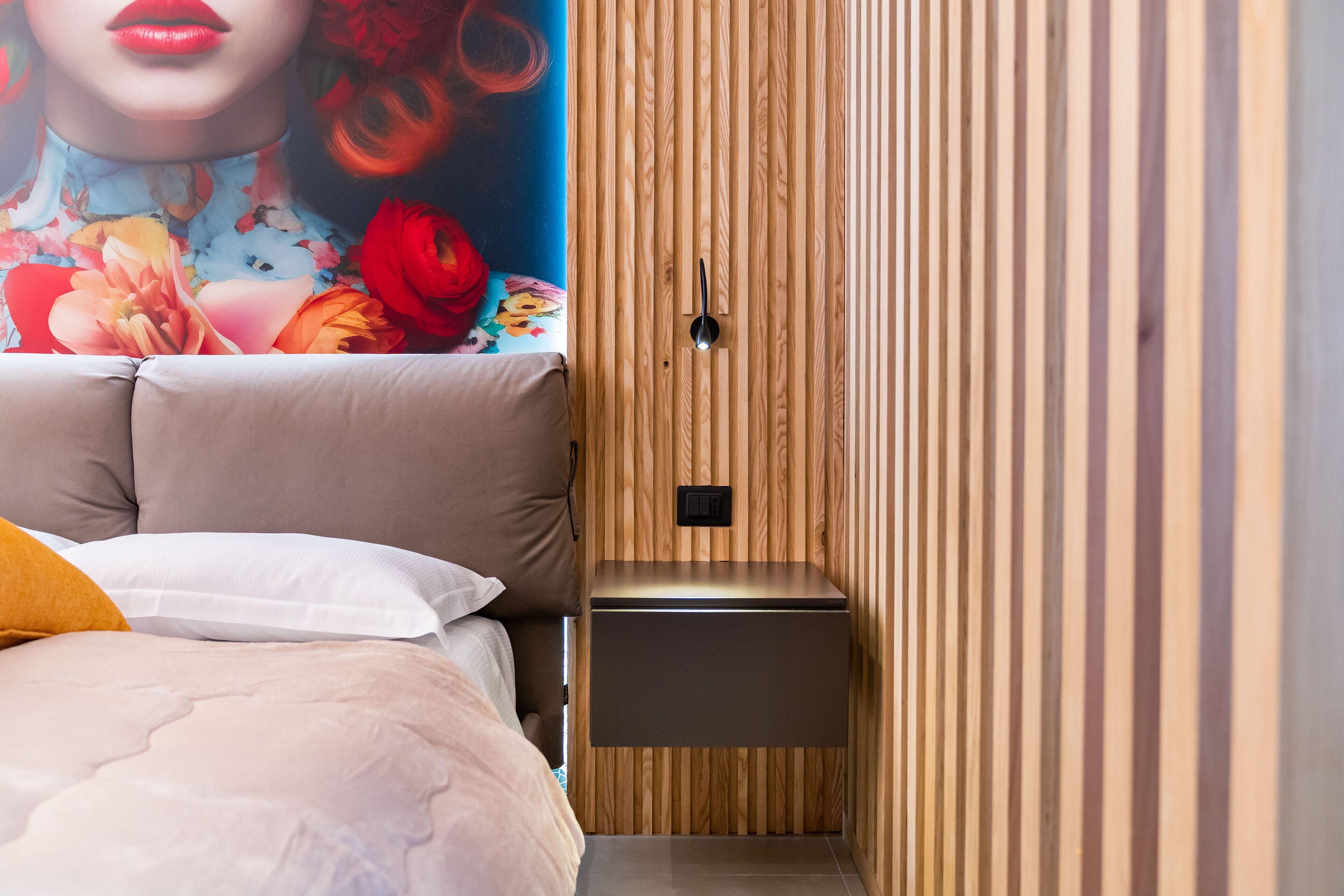 A bedroom with a bed, a nightstand, a wooden wardrobe, and a mural on the wall.