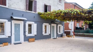 Fila de portes amb persianes, un pati pavimentat i un edifici amb façana gris.