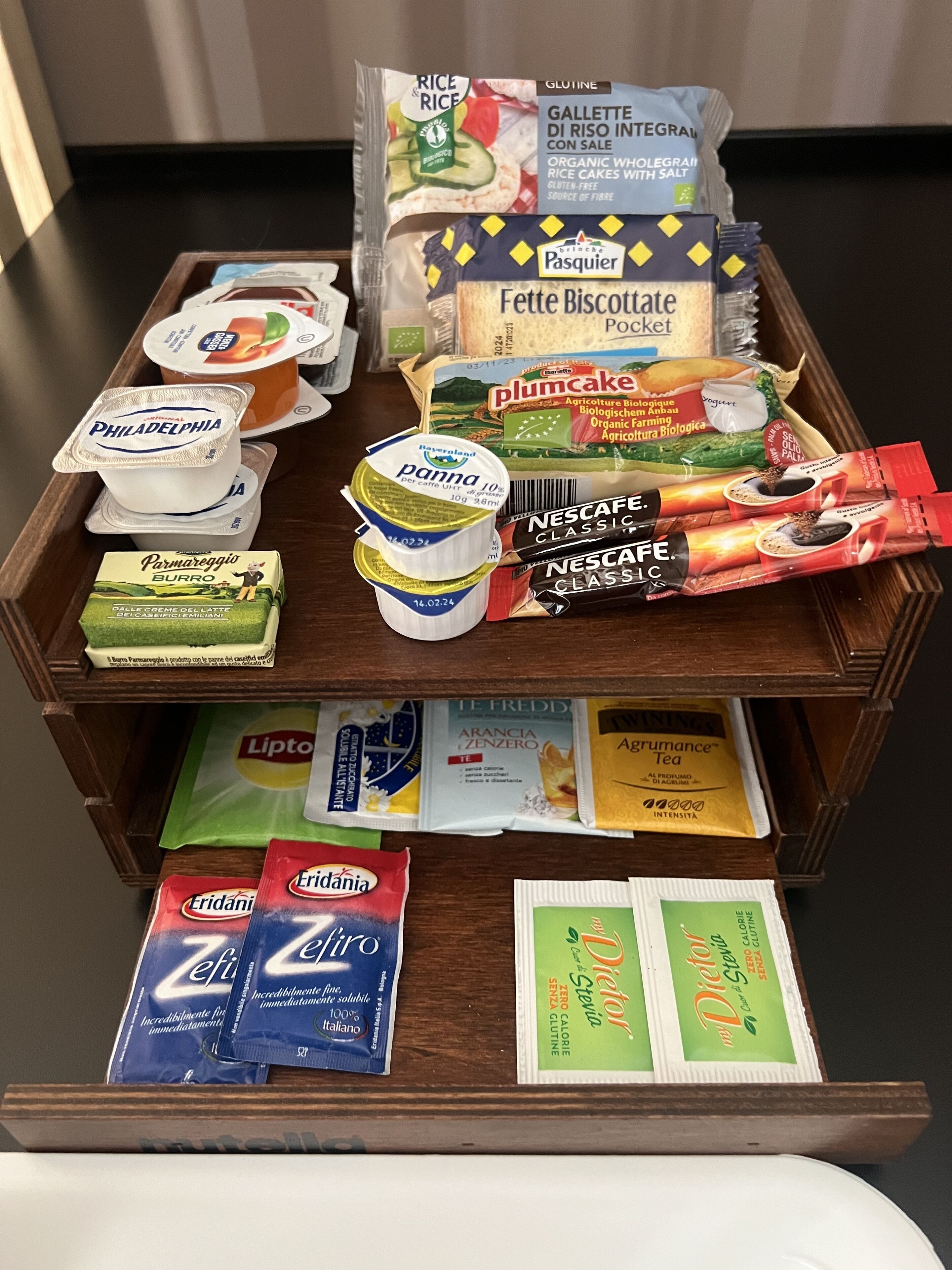 A wooden display case with various food items including rice cakes, biscuits, yogurt, and tea.