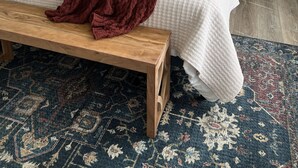 Ein ordentlich eingerichtetes Schlafzimmer mit einem Bett, zwei Nachttischen, einer Bank und einem gemusterten Teppich.
