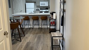 Eine moderne Küche mit grauen Schränken, einer weißen Arbeitsplatte und einer zentralen Kochinsel mit Barhocker.