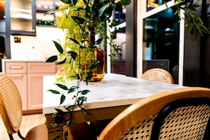 A dining table with chairs, a vase with flowers, and a kitchen area in the background.
