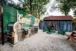 A patio area with a stainless steel grill, green chairs, and a rustic wooden shelter.