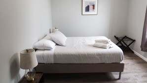 A neatly made bed with pillows and folded towels, a bedside lamp, and a framed picture on the wall. - 3Bed 2Bath Apt Near NYC + Parking & Laundry (Irvington)