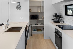 A modern kitchen with white cabinetry, a built-in microwave, a coffee machine, and a black oven.