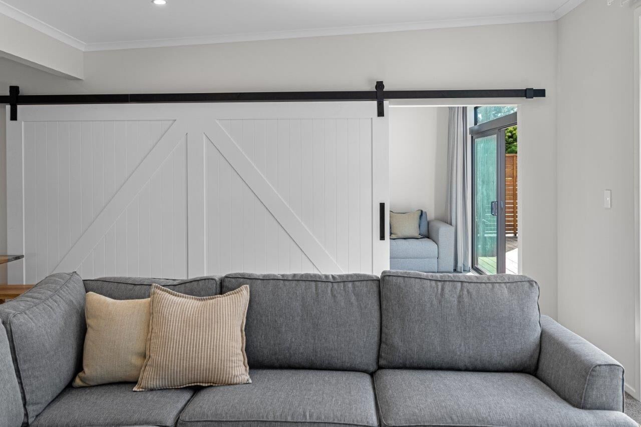 A grey sofa with two pillows in a room with a white sliding barn door and a view of an outdoor area.