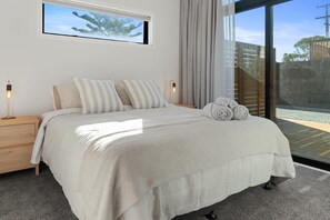 A bedroom with a large bed, a nightstand, a window with a view of trees, and a curtain.