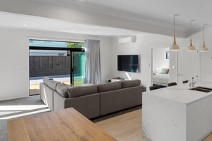 A modern living space with a sofa, a wooden dining table, a kitchen island, and a TV mounted on the wall.