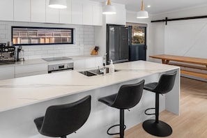 A modern kitchen with a large island, bar stools, and a dining table. - Decked out on Leo (Waihi Beach)
