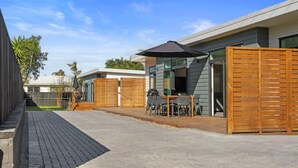 Un'area patio esterna moderna con tavolo e sedie, un barbecue e una recinzione in legno.