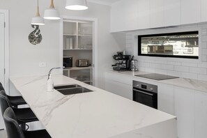 A modern kitchen with a marble countertop, built-in oven, and a coffee machine.