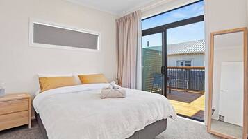 A bedroom with a large bed, a nightstand, a sliding glass door to a balcony, and a view of a building outside.