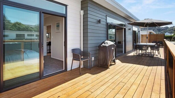 En moderne udendørs terrasse med en skydedør, der fører til et soveværelse, en grill og et spiseområde med havemøbler.