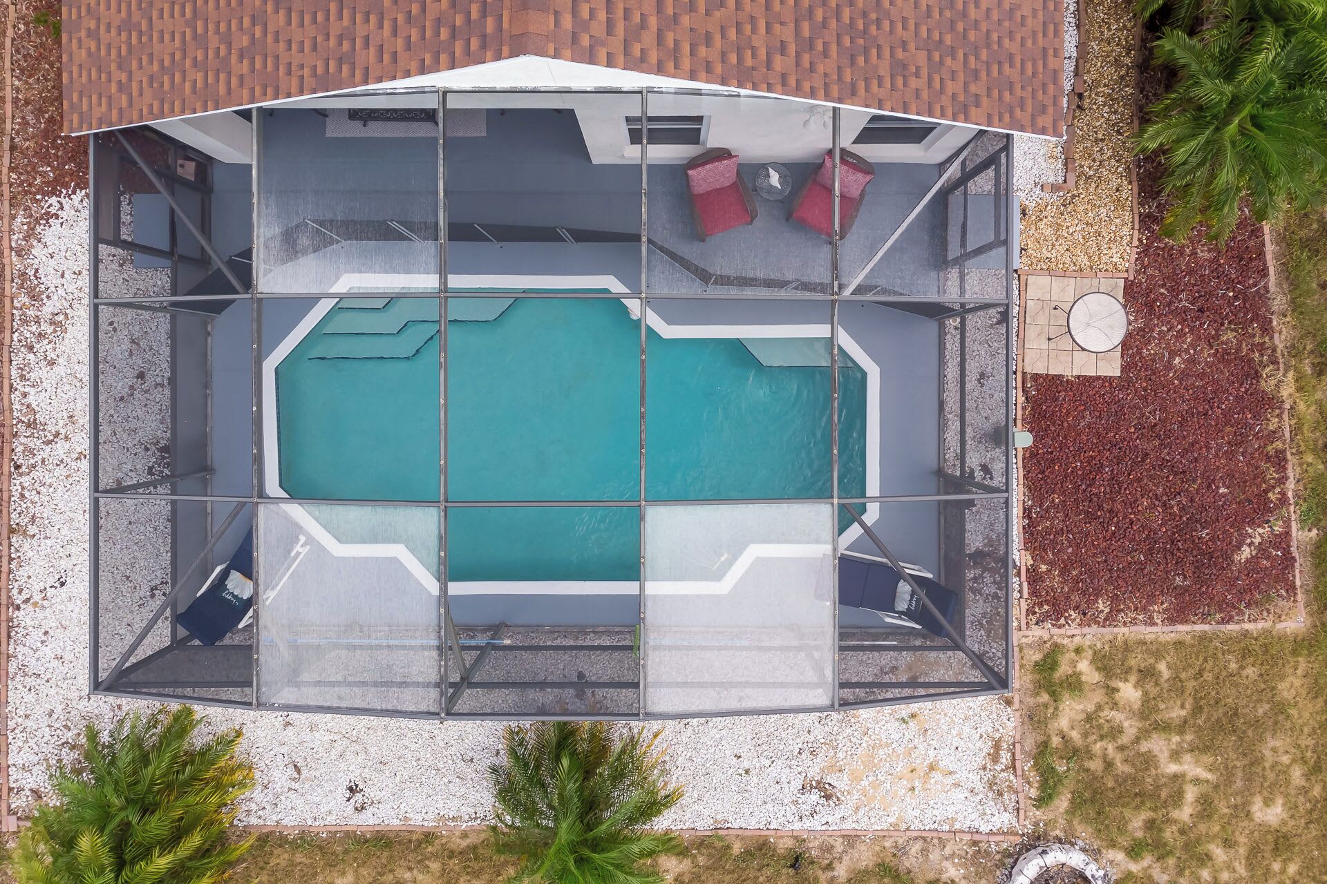 An aerial view of a covered swimming pool with a glass enclosure, surrounded by a brick patio and small trees.