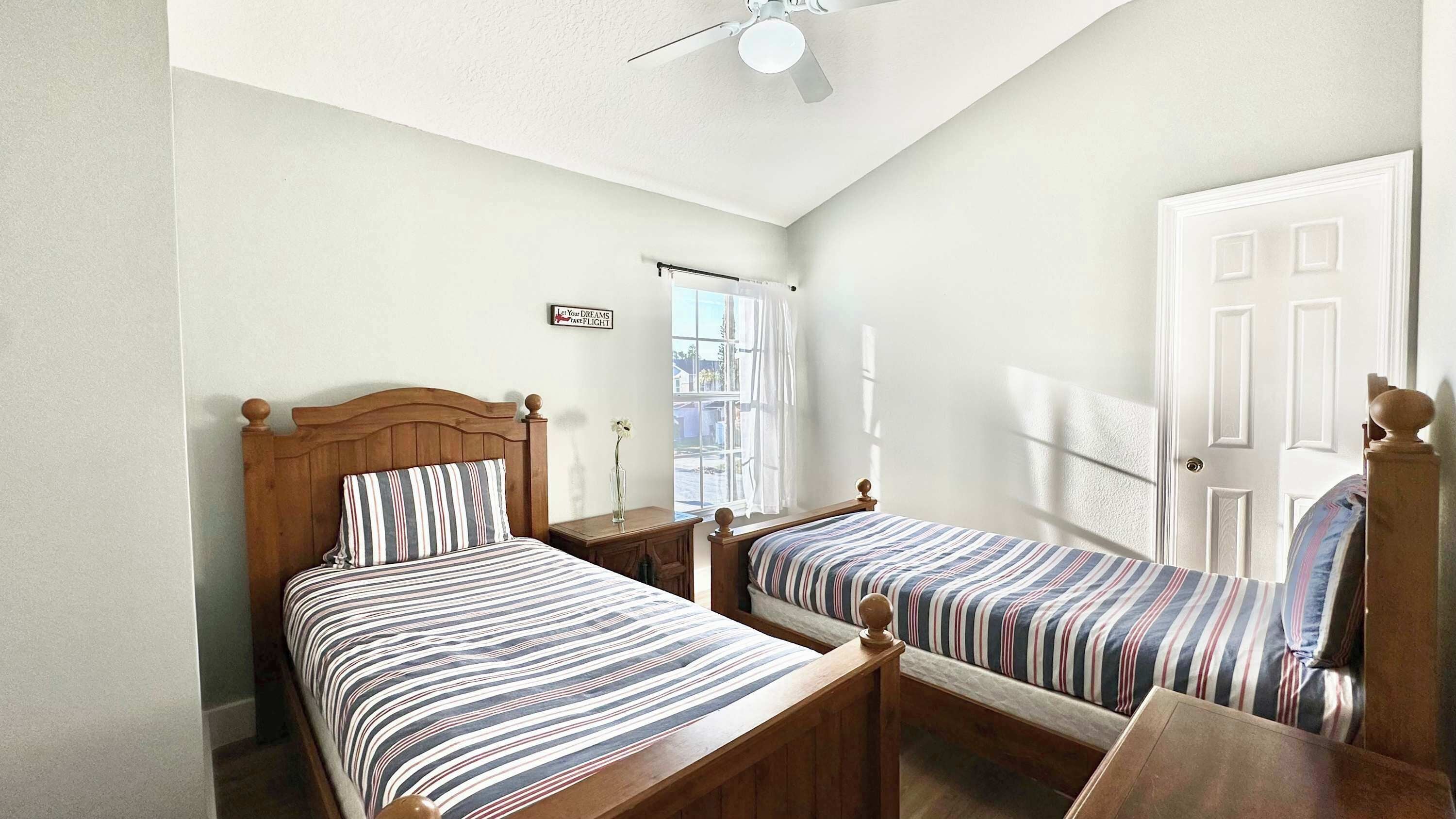 A bedroom with two wooden beds, a ceiling fan, a window with a view, and a door.