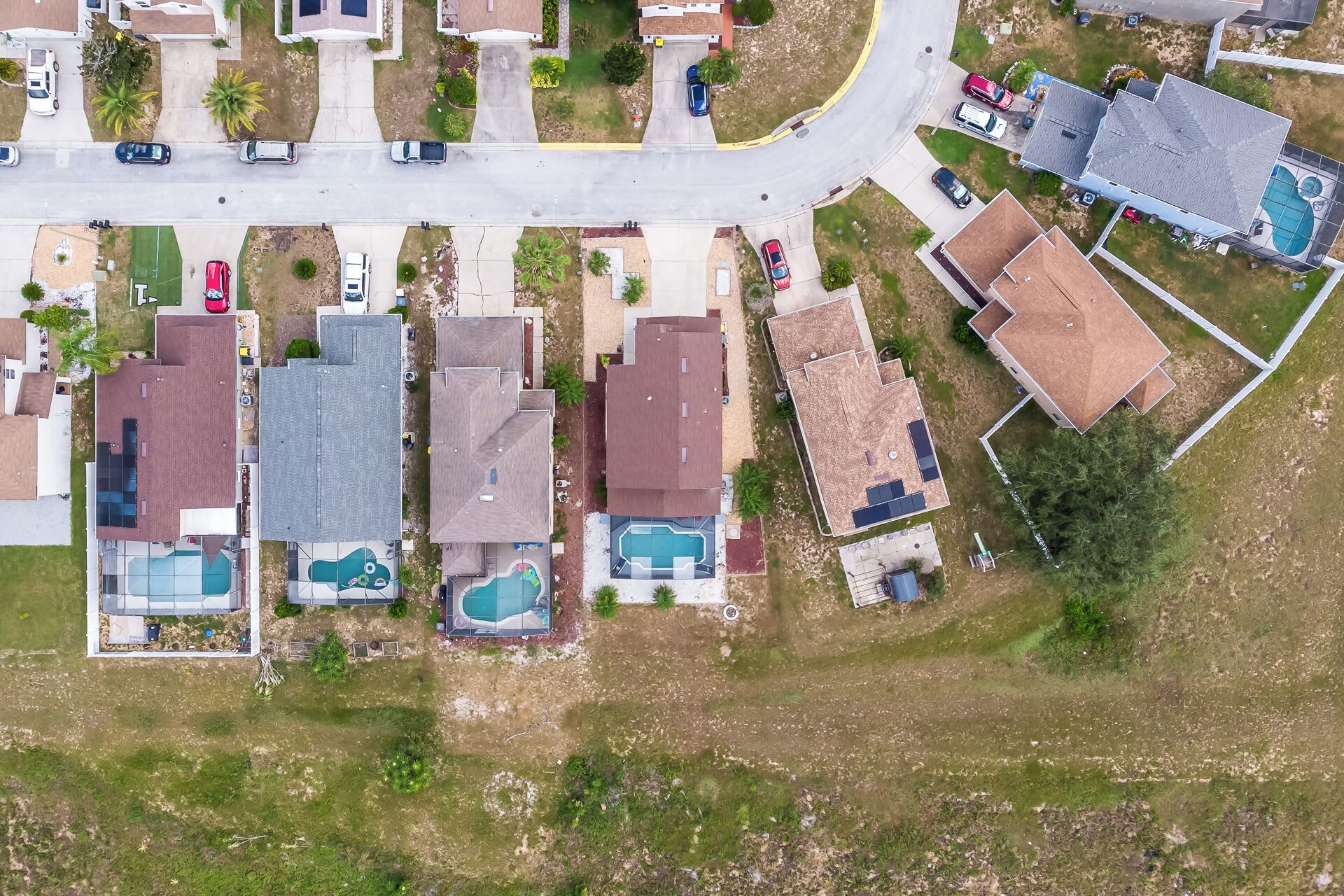 An aerial view of a residential area with houses, a road, and a swimming pool.