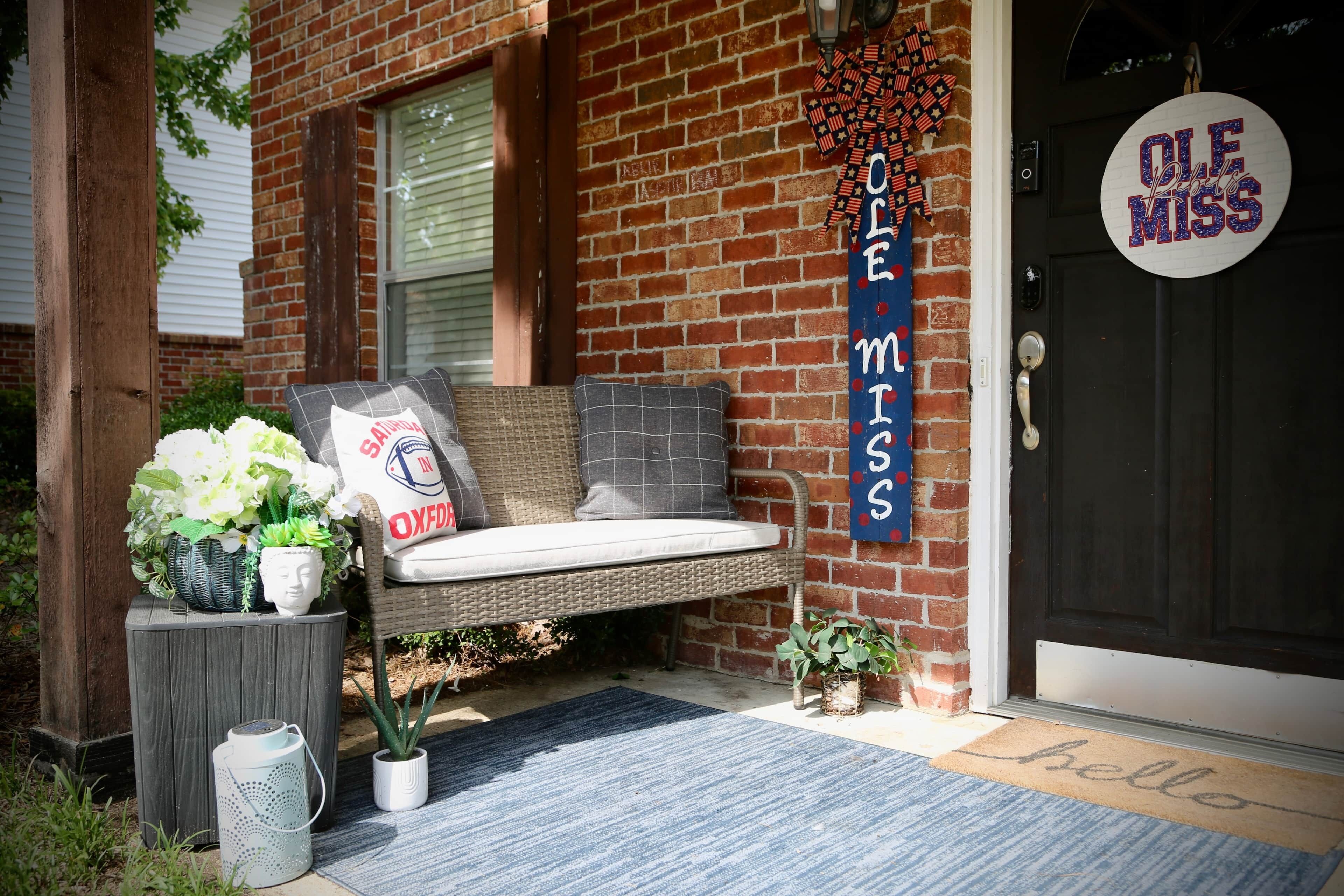 A front porch with a bench, a welcome mat, and a door with a sign reading 'Ole Miss'.
