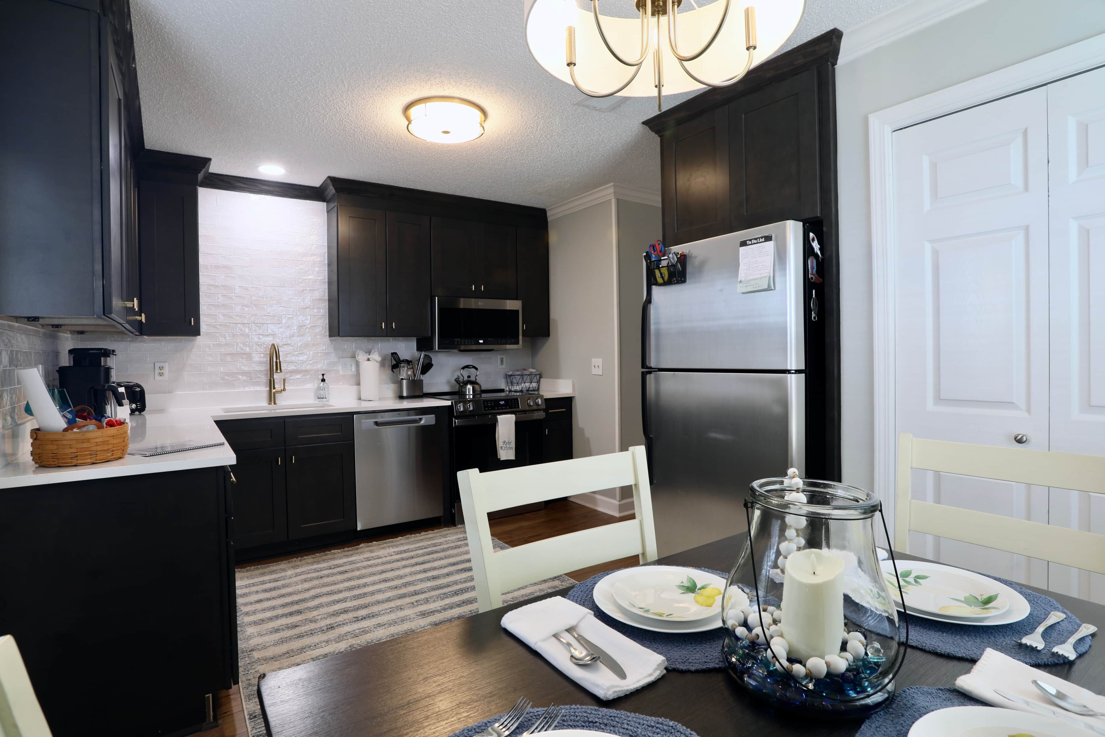 A modern kitchen with dark cabinetry, stainless steel appliances, and a dining area set for a meal.