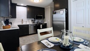 A modern kitchen with dark cabinetry, stainless steel appliances, and a dining area set for a meal. -  Book The Drew - a rare find, only a 20 minute walk to the Grove and Campus  (Oxford)
