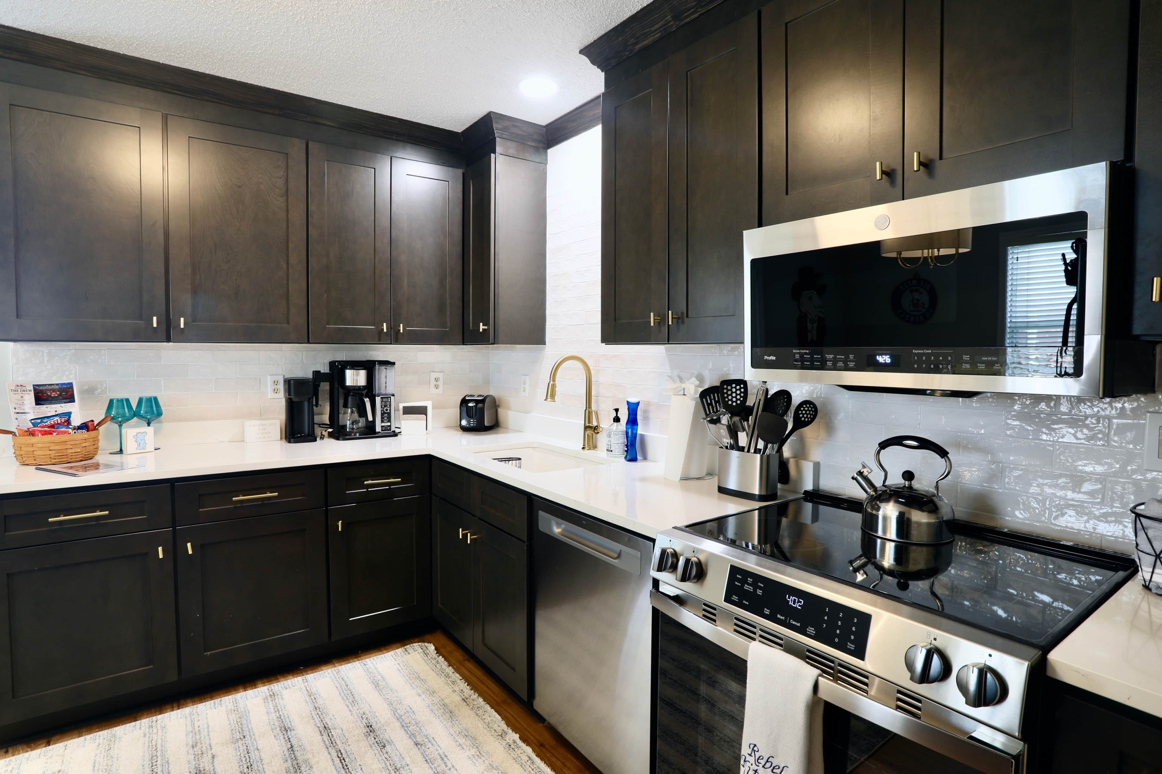A modern kitchen with dark cabinets, a stainless steel range, and a microwave.