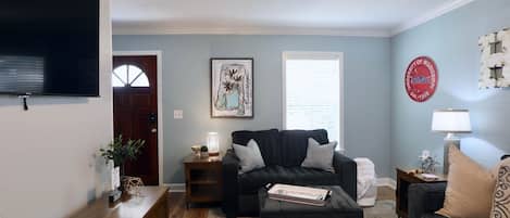 A living room with a dark grey sofa, a wooden coffee table, a ceiling fan, and a wall-mounted TV.