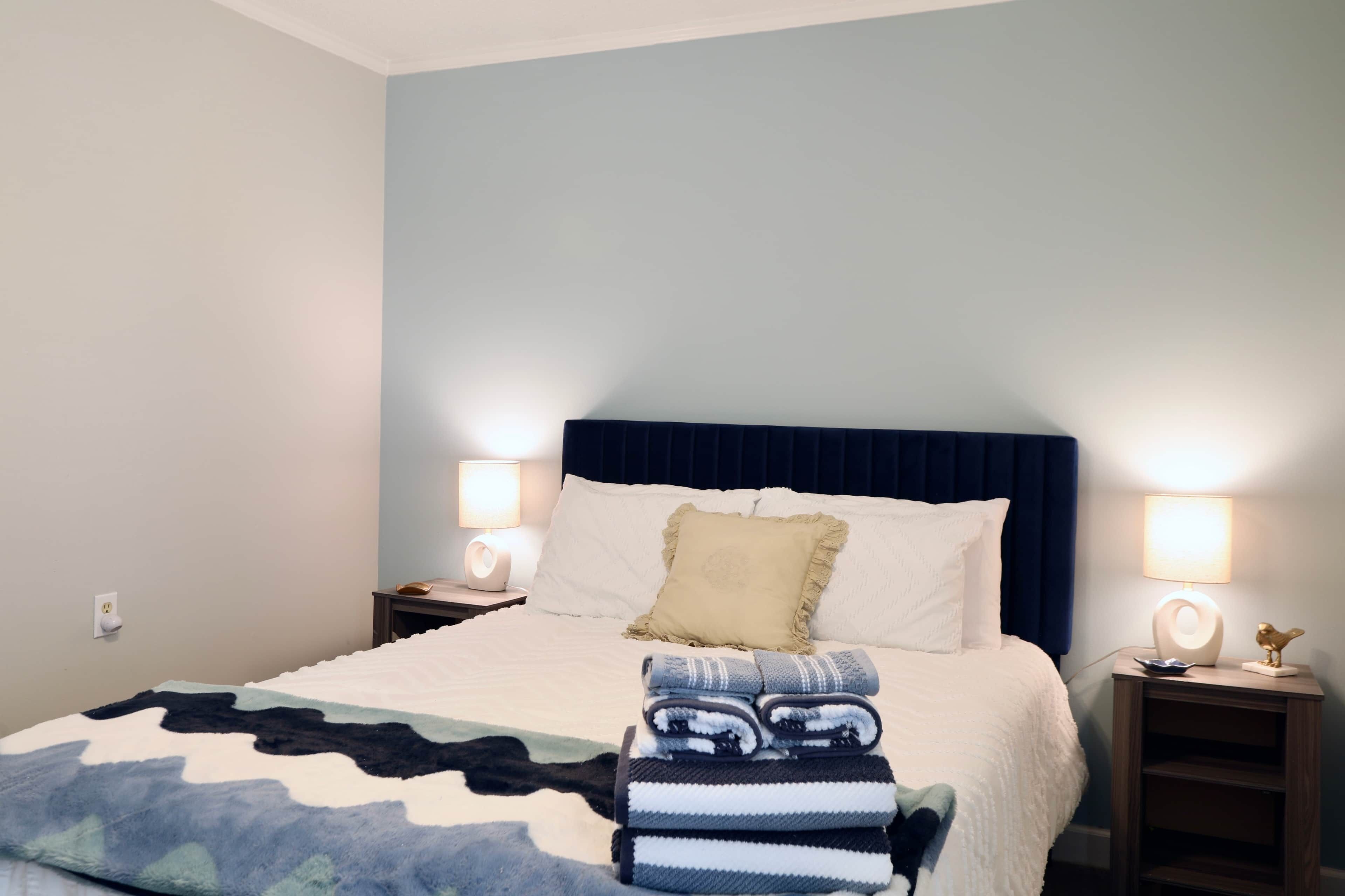 A neatly made bed with a blue headboard, two bedside lamps, and a folded blanket on the bed.