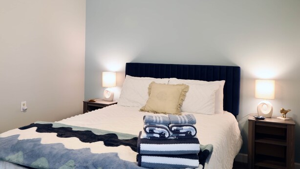 A neatly made bed with a blue headboard, two bedside lamps, and a folded blanket on the bed. -  Book The Drew - a rare find, only a 20 minute walk to the Grove and Campus  (Oxford)