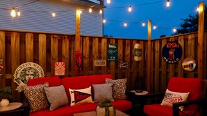 An outdoor seating area with a red sofa and chairs, string lights, and various signs and decorations on a wooden fence. -  Book The Drew - a rare find, only a 20 minute walk to the Grove and Campus  (Oxford)