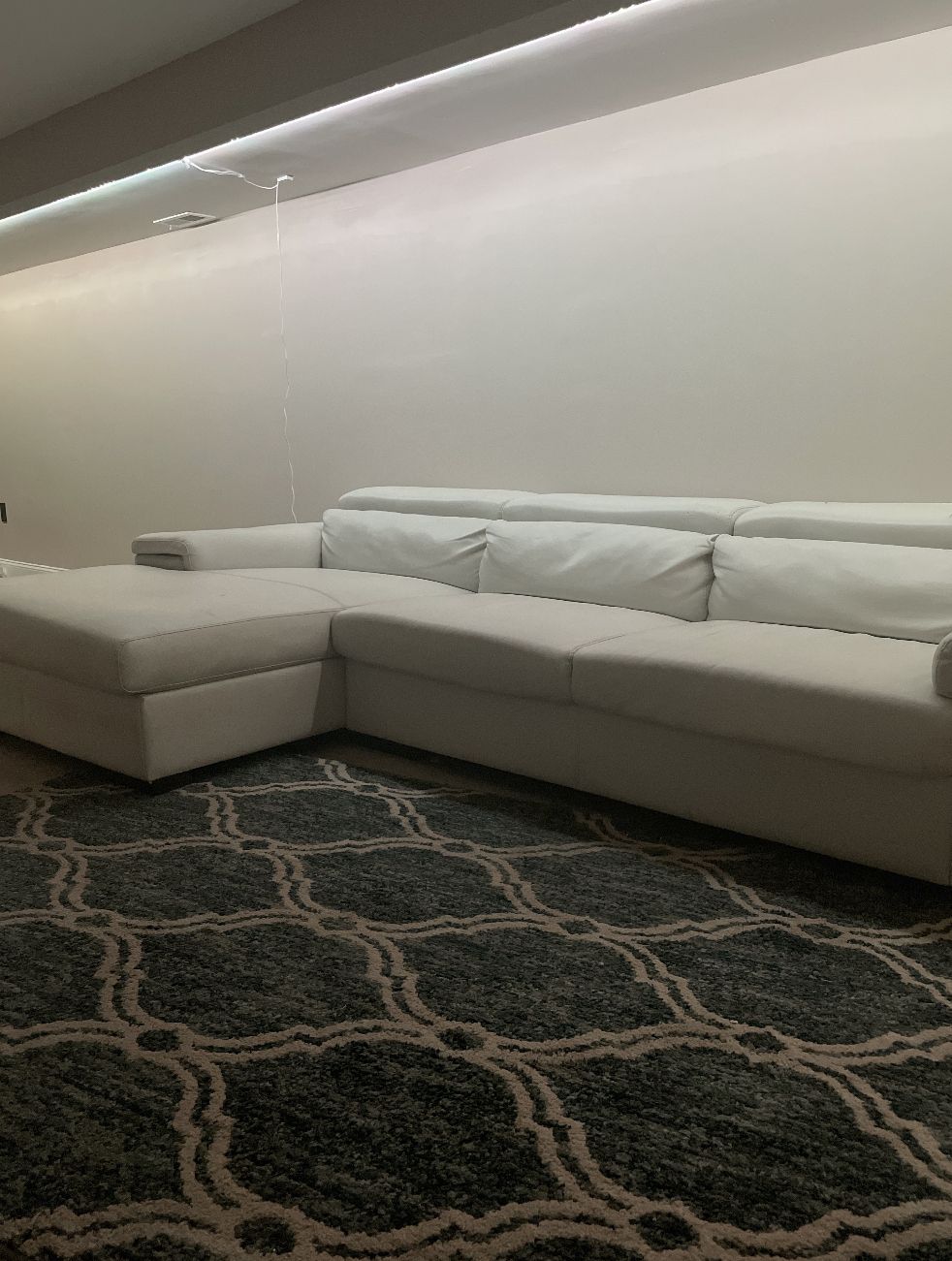 A room with a sectional sofa, a patterned rug, and a ceiling light fixture.