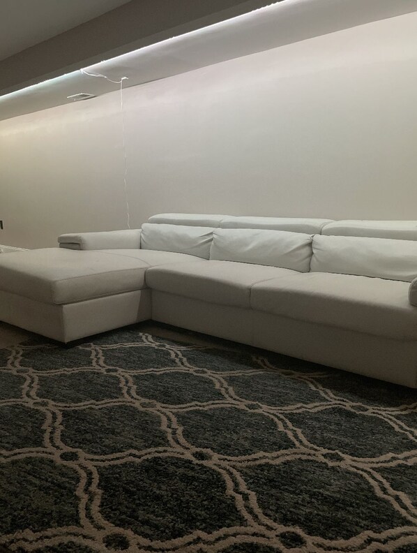 A room with a sectional sofa, a patterned rug, and a ceiling light fixture.