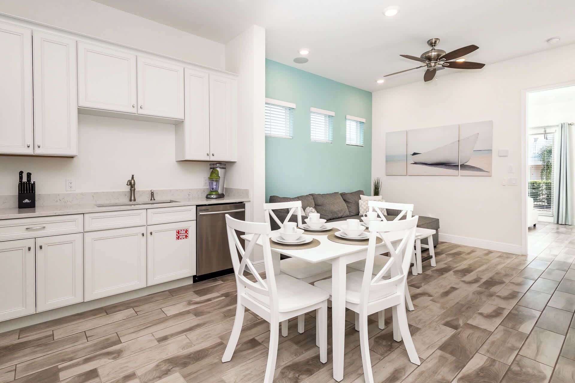 Une cuisine moderne avec des meubles blancs, un coin repas avec des chaises blanches et un ventilateur de plafond.