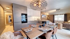 A modern kitchen with built-in appliances, a dining area with a wooden table set for four, and a large pendant light.