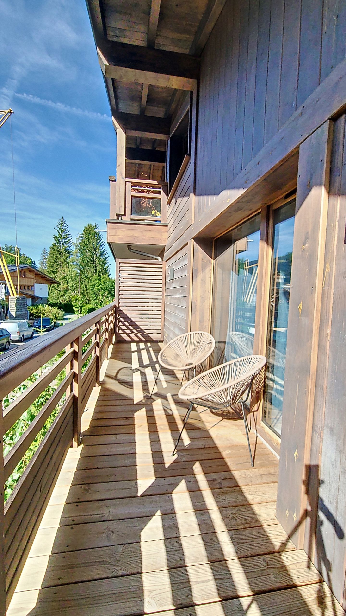 A wooden deck with a railing, two wicker chairs, and a glass door leading to a balcony.